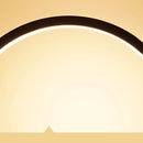 Eine stilvolle 'CircoloLuce' Nachttischlampe in minimalistischem Design leuchtet auf einem Nachttisch, neben einer Vase mit Zweigen.