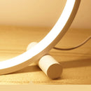 Eine stilvolle 'CircoloLuce' Nachttischlampe in minimalistischem Design leuchtet auf einem Nachttisch, neben einer Vase mit Zweigen.