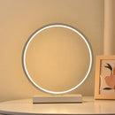 Modern Luce dell'Anello bedside lamp with circular LED light and minimalist design on a bedside table.