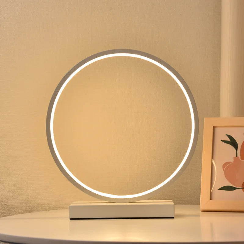Modern Luce dell'Anello bedside lamp with circular LED light and minimalist design on a bedside table.