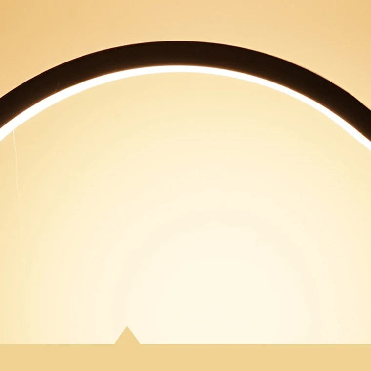 A stylish 'CircoloLuce' bedside lamp in a minimalist design shines on a bedside table, next to a vase with branches.