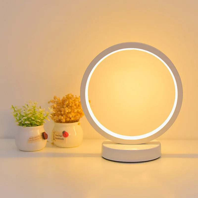Modern Luce dell'Anello bedside lamp with circular LED light and minimalist design on a bedside table.